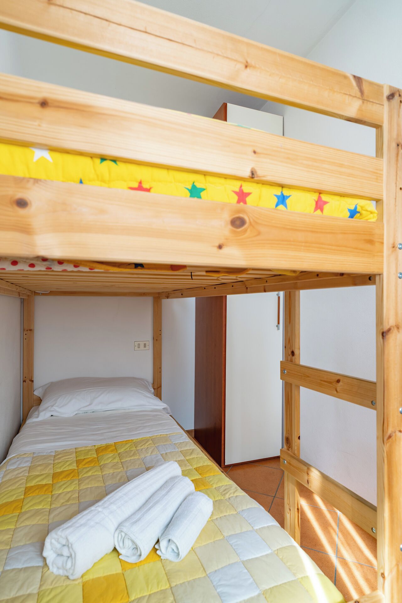 A bunk bed with a yellow and white quilt, a wooden frame, and a star decoration on the top bunk.