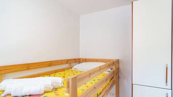 A small, single-bed room with a wooden bunk bed, a white wardrobe, and a colorful bedspread.