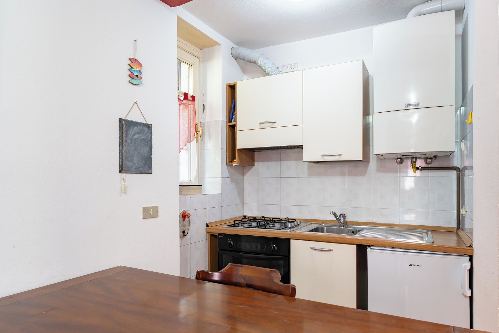 A compact kitchen with white cabinets, a gas stove, a sink, and a small refrigerator.