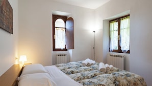 A bedroom with a bed, two windows with curtains, a floor lamp, and a radiator. - The Court of the moon (Barzio)