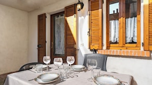A dining table set with plates, glasses, and cutlery, positioned under a window with wooden shutters. - The Court of the moon (Barzio)