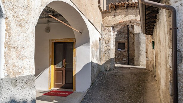 A narrow alleyway with a stone building, a wooden door, and a red mat with "CONFORT" written on it. - The Court of the moon (Barzio)