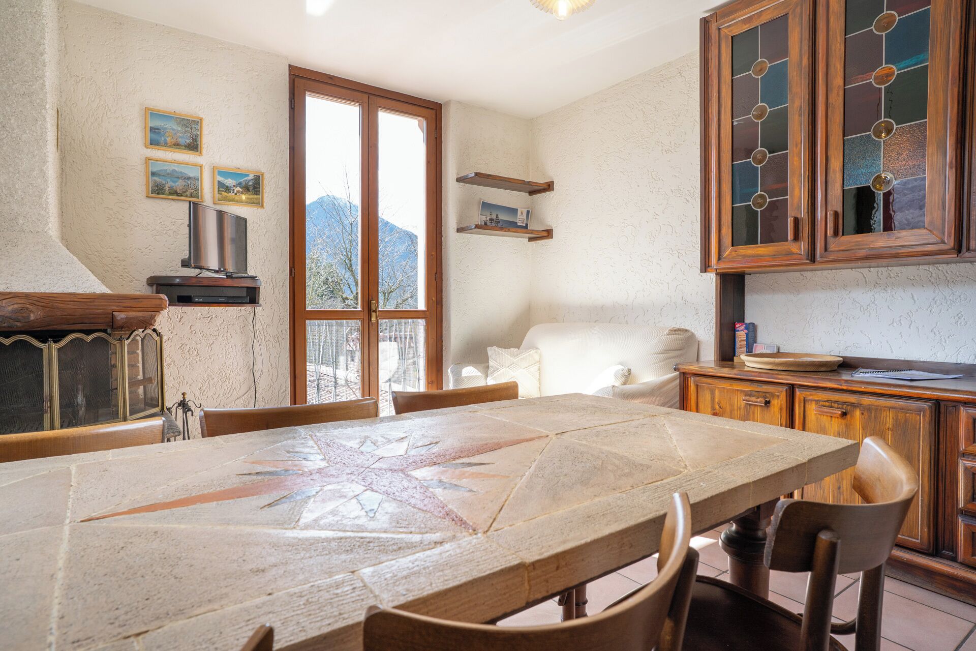 Een gezellige keuken met een grote eettafel, houten kasten en uitzicht op bergen door het raam.