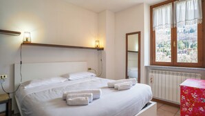 A hotel room with a bed, bedside lamps, a window with a view, and a red floral table. - Mountain lodging with mountain view (Barzio)