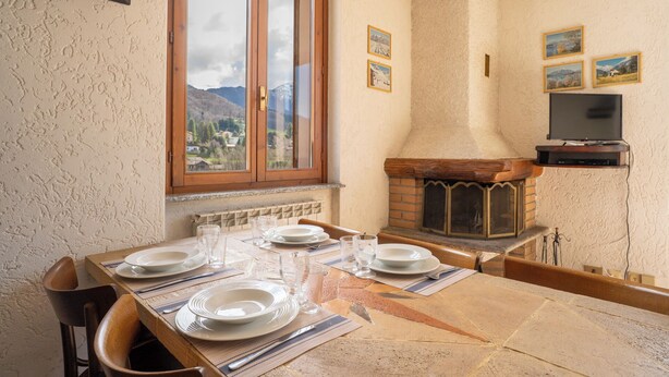 A dining area with a table set for four, a fireplace, and a television mounted on the wall. - Mountain lodging with mountain view (Barzio)
