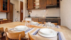 A dining area with a table set for two, wooden cabinets, a kitchen in the background, and a tiled backsplash. - Mountain lodging with mountain view (Barzio)