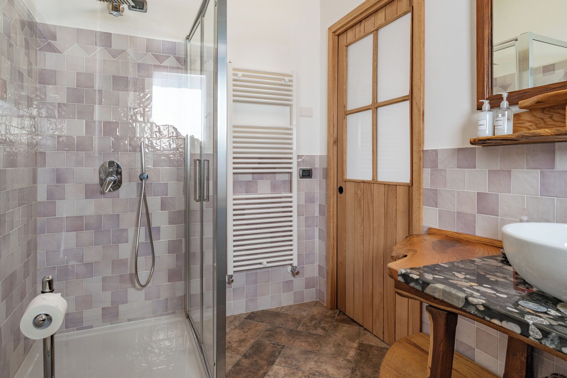 Ein Badezimmer mit Dusche, einer Holztür, einem Waschbecken mit Marmorplatte und einem Spiegel darüber.