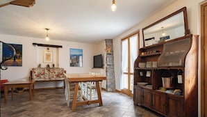 A cozy living room with a wooden table, a sofa, a stone pillar, and a wooden cabinet with kitchen utensils. - Ballabio Lake - Rustic Chic Retreat (Ballabio)