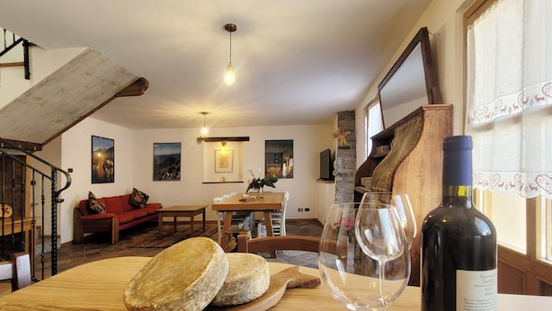 A rustic interior with a wooden staircase, a dining area with a table and chairs, a sofa, and a wine bottle on a table. - Ballabio Lake - Rustic Chic Retreat (Ballabio)