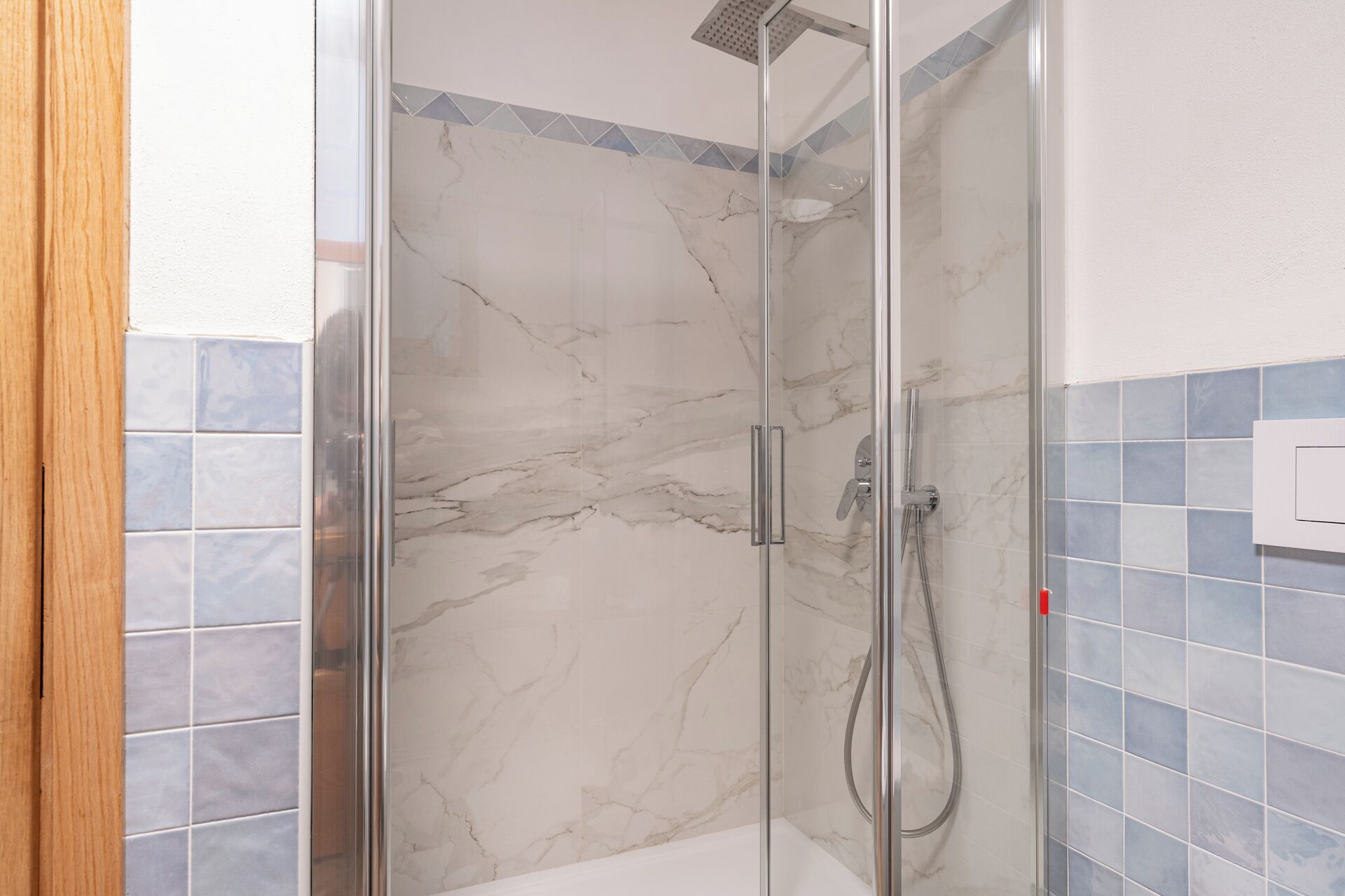 A glass-enclosed shower with a marble wall, a showerhead, and a handheld showerhead.