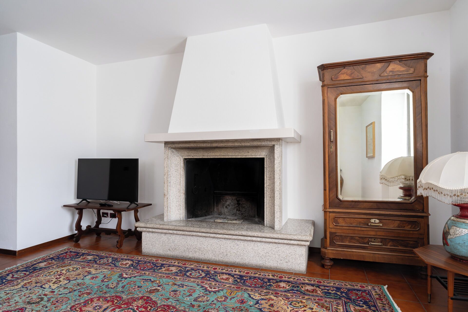 A room with a fireplace, a large mirror, and a traditional wooden cabinet.