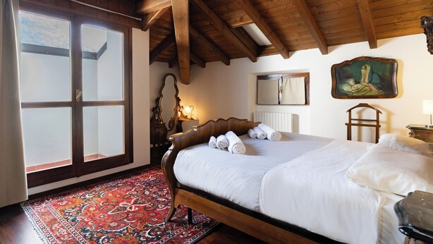 Une chambre avec un grand lit, un plafond en bois, une fenêtre avec des rideaux, un tapis à motifs et un tableau accroché au mur.