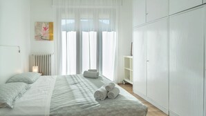 A bedroom with a bed, a radiator, a window with sheer curtains, and a wardrobe.