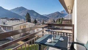 A balcony with a table and chairs, overlooking a mountainous landscape with buildings in the distance.