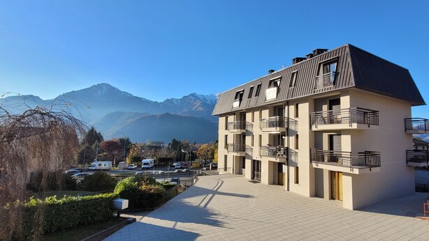 A modern multi-story building with balconies, situated in a mountainous area with clear skies.