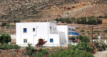 Um edifício branco com detalhes em azul, uma varanda e montanhas ao fundo.