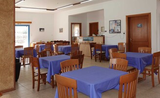 Uma sala de jantar com várias mesas cobertas por toalhas azuis e cadeiras de madeira.