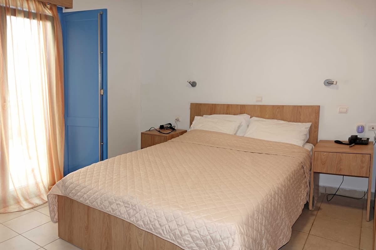 A neatly arranged hotel room with a bed, bedside tables, a phone, and a curtain.