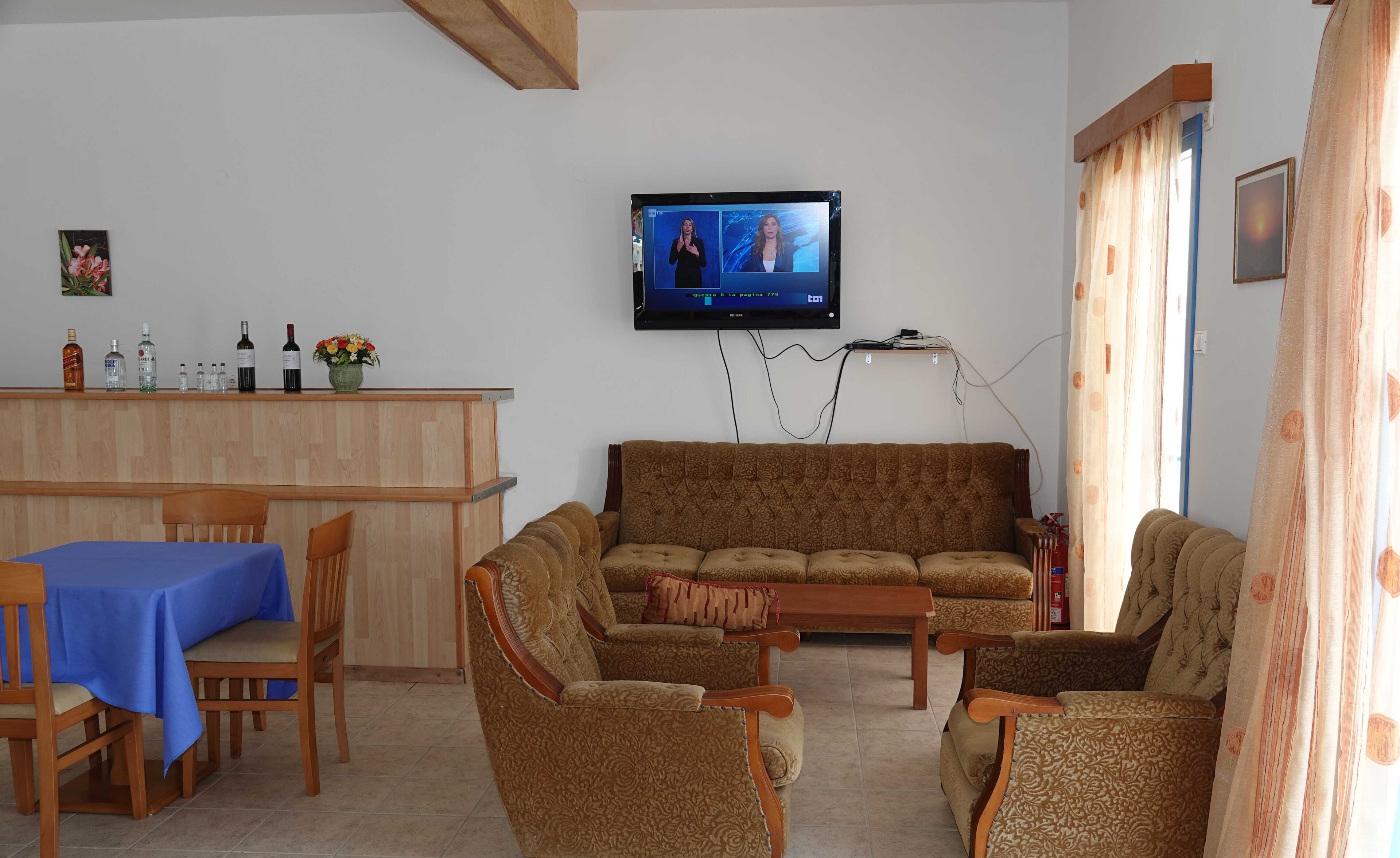 Een woonkamer met een bank, stoelen, een salontafel, een televisie en een barruimte met flessen en een bloevas.