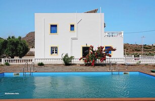 Um edifício branco com detalhes azuis e uma piscina em frente.
