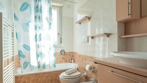 A bathroom with a bathtub, toilet, sink, and a shower curtain with a leaf pattern.