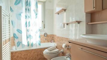 Un bagno con vasca, WC, lavandino e tenda da doccia a motivi floreali.