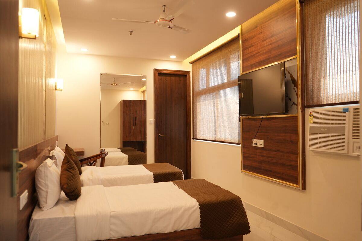 A hotel room with two beds, a ceiling fan, a TV, and an air conditioning unit.