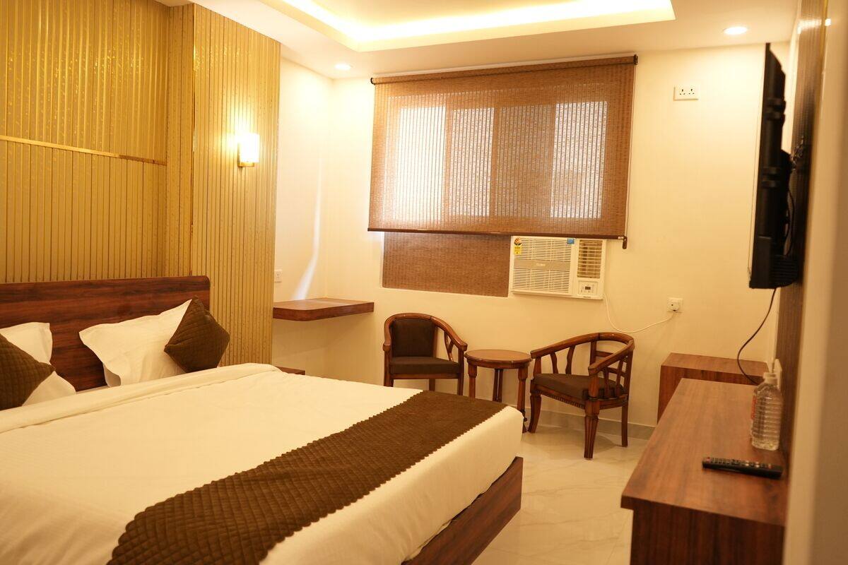 A hotel room with a bed, a desk, two chairs, a television, and an air conditioning unit.