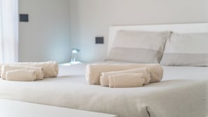Siististi pedattu sänky, siististi taitellut pyyhkeet ja yöpöytä hotellihuoneessa.