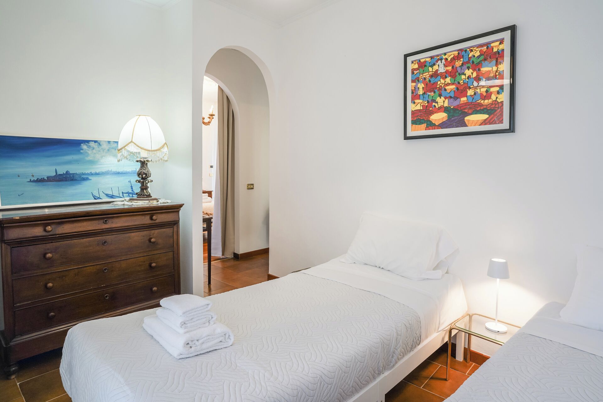 Una camera d'albergo con un letto, una cassettiera, un quadro e una lampada.