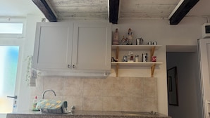 Een keuken met witte kastjes, een granieten aanrechtblad en een tegelwand van baksteen. Boven het aanrecht staan planken met keukenspullen.
