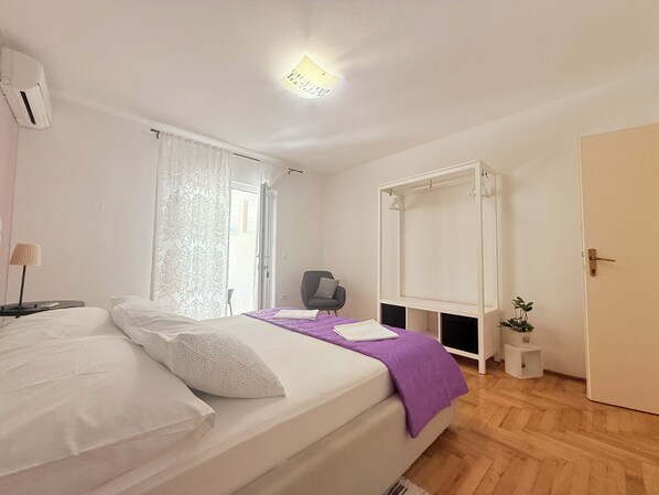 Un dormitorio con cama, una silla, un armario y una mesita con una planta.
