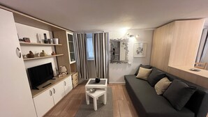 A modern living room with a flat-screen TV, a sofa, a coffee table, and a dining area with a table and chairs. - Bellano Studio 2 - Studio Apartment, Sleeps 2 (Bellano)