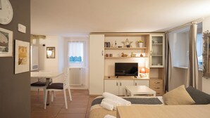 A compact hotel room with a bed, a desk, a TV, and a small kitchenette. - Bellano Studio 2 - Studio Apartment, Sleeps 2 (Bellano)