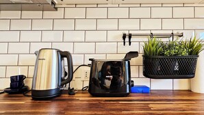 Ett kök med kakel ovanför arbetsbänken, en kaffebryggare, en vattenkokare och en hängande växt.