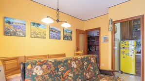 A living room with a sofa, a dining table, and a kitchen area with a yellow refrigerator.