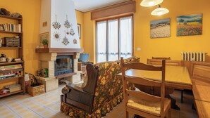 A cozy living room with a fireplace, a dining area with a wooden table and chairs, and a bookshelf filled with books and decorative items.