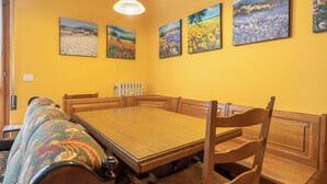 A dining area with a wooden table and benches, yellow walls, and floral paintings.