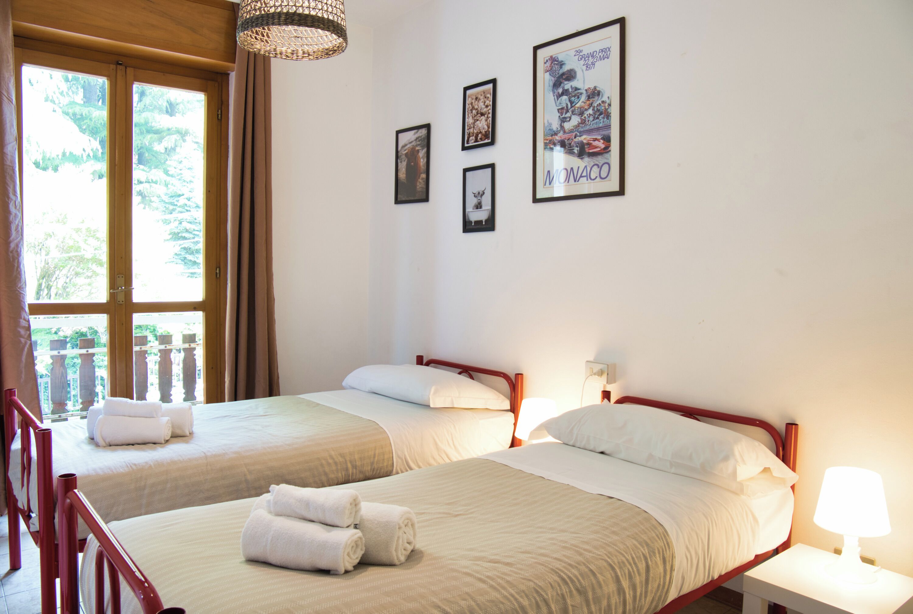 A hotel room with two beds, a balcony, and a poster of Monaco.