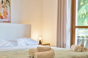 A neatly made bed with rolled towels, a bedside lamp, and a window with curtains.