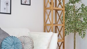 Un sofá blanco con almohadones decorativos, un separador de madera enrejada y una planta en maceta.