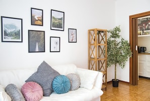 A white sofa with decorative pillows, a wooden plant stand, and framed pictures on the wall.