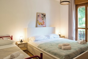 A hotel room with a bed, a bedside table with a lamp, a window with curtains, and a painting on the wall.