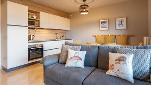 Eine moderne Küche mit weißen Schränken, einem eingebauten Backofen und einer Mikrowelle. Es gibt ein graues Sofa mit Zierkissen sowie eine Essecke mit Tisch und Stühlen.