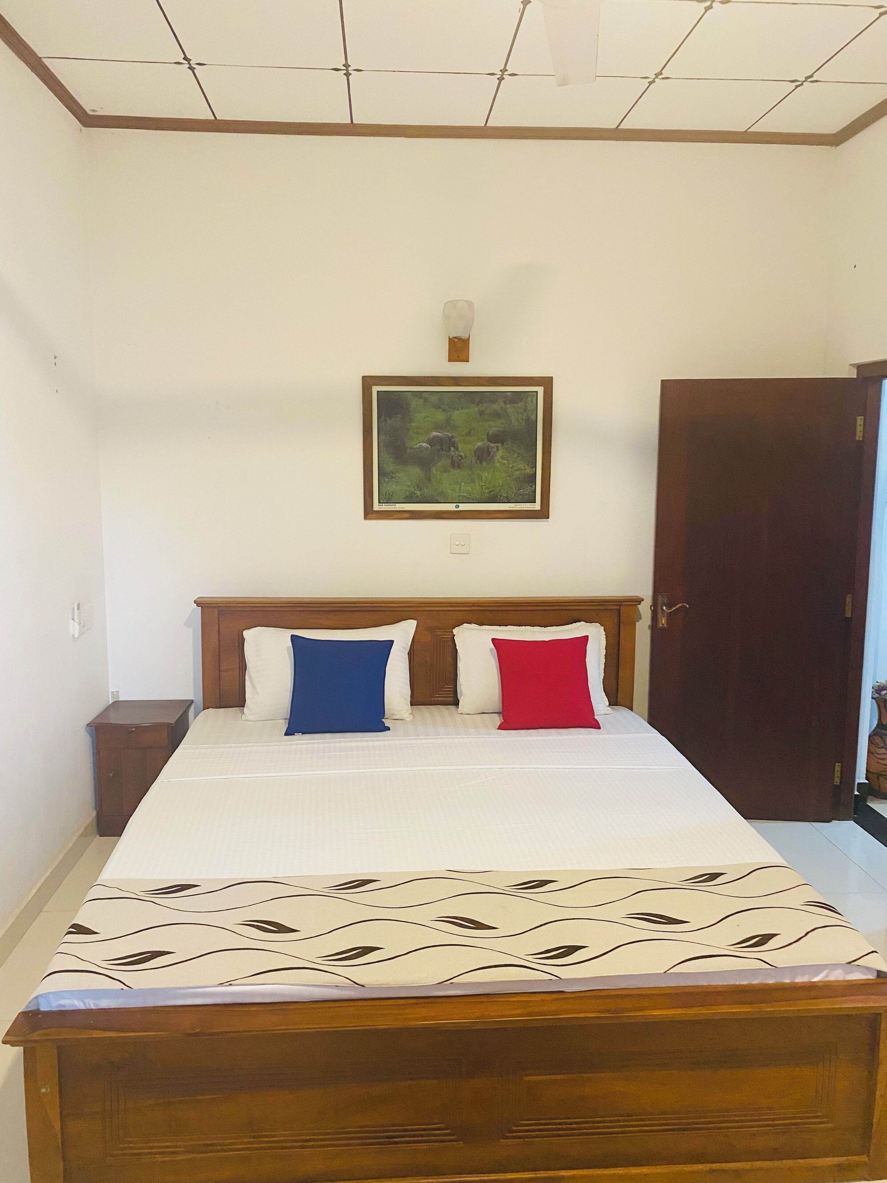 A bedroom with a bed, two nightstands, a wooden headboard, a painting, and a door.