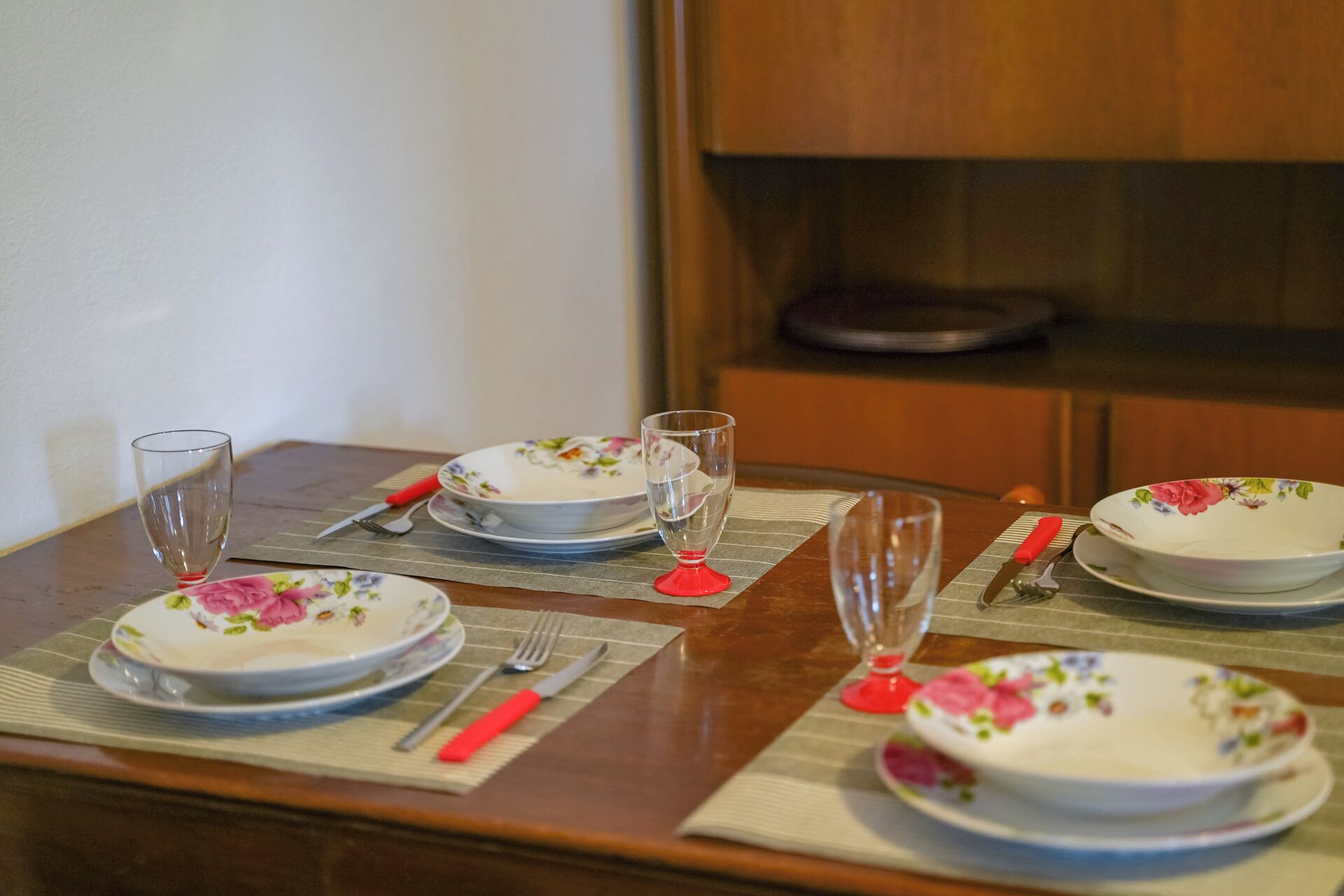 A dining table set with floral plates, red-handled cutlery, and clear drinking glasses.