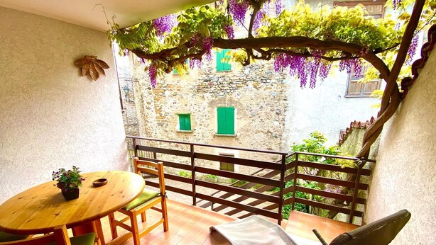 Eine Terrasse mit Holztisch und -stühlen, einem Hängesessel und einer Steinmauer mit einem Fenster.