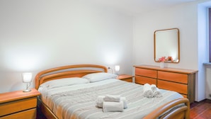 Una cama bien hecha con una colcha a rayas, dos lámparas de noche, un tocador de madera, un espejo y dos toallas enrolladas sobre la cama.