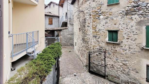 Una estrecha calle adoquinada bordeada por edificios de piedra con balcones y una entrada con reja.