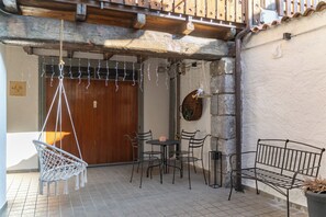 Een terras met een houten deur, een hangstoel en metalen meubilair.